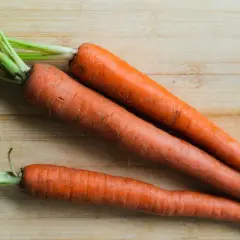 Trzy świeże marchewki z zielonymi naćmi leżą na drewnianej desce. Czy pies może jeść codziennie marchew?