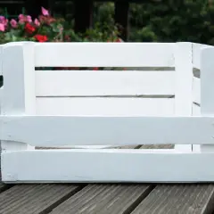 Biała drewniana skrzynka, idealna baza, by dowiedzieć się, jak zrobić legowisko dla kota. W tle kwitnące kwiaty.