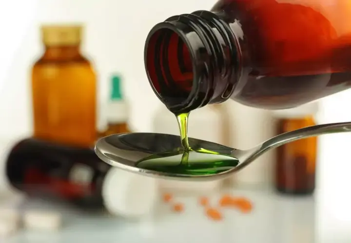 Zielony syrop prawoślazowy dla psa kapie z butelki na łyżkę. W tle widać inne leki.