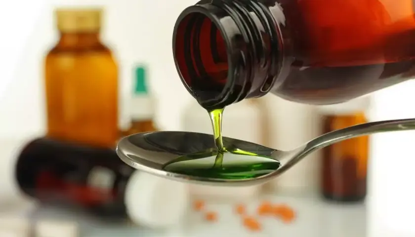 Zielony syrop prawoślazowy dla psa kapie z butelki na łyżkę. W tle widać inne leki.