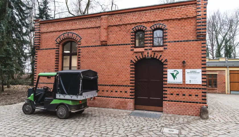 Zielony wózek golfowy przed ceglanym budynkiem gabinetu weterynaryjnego w zoo.