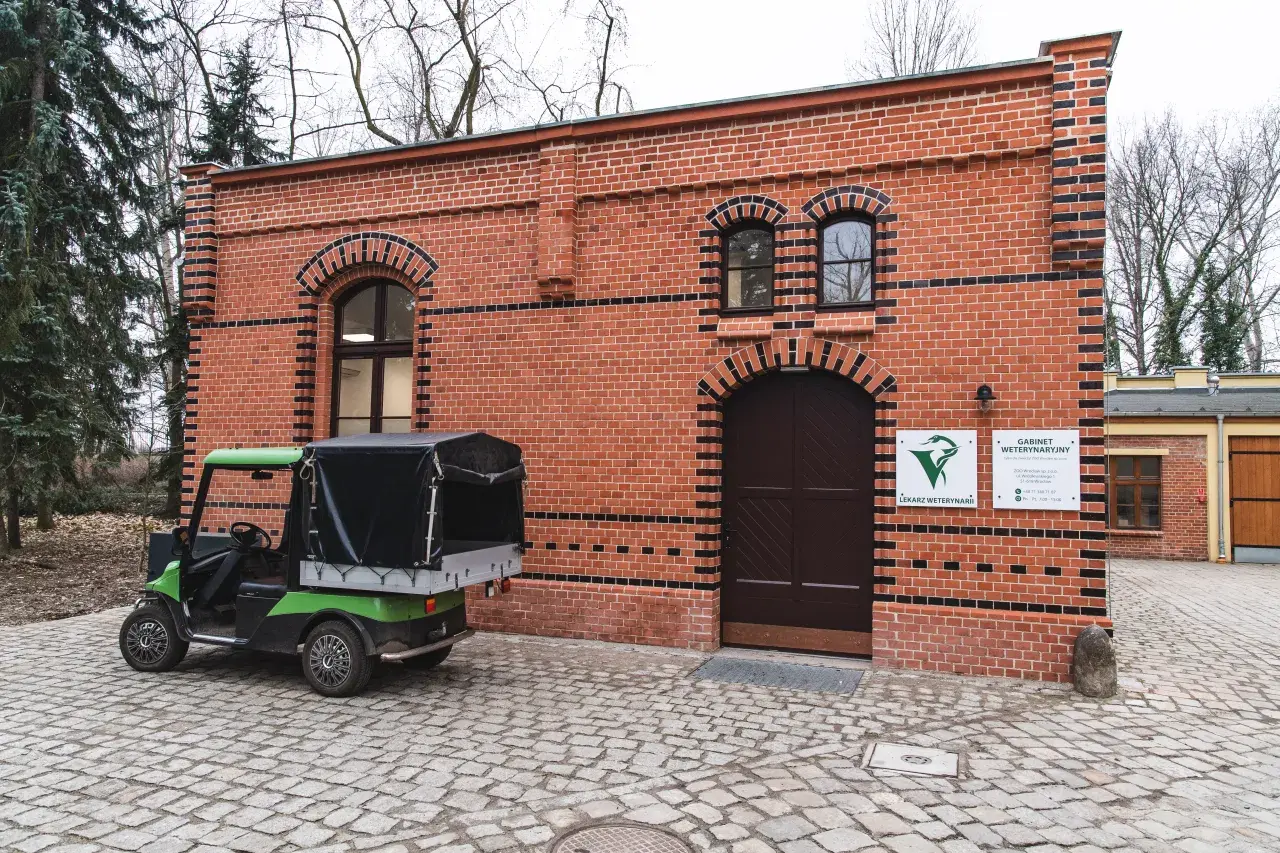 Zielony wózek golfowy przed ceglanym budynkiem gabinetu weterynaryjnego w zoo.