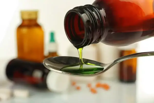 Zielony syrop prawoślazowy dla psa kapie z butelki na łyżkę. W tle widać inne leki.
